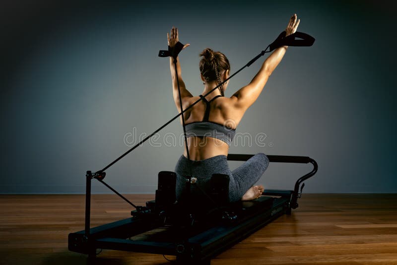 Menina fazendo exercícios de pilotagem com cama reformadora Belo treinador de ginástica fino em fundo cinza reformador, baixo