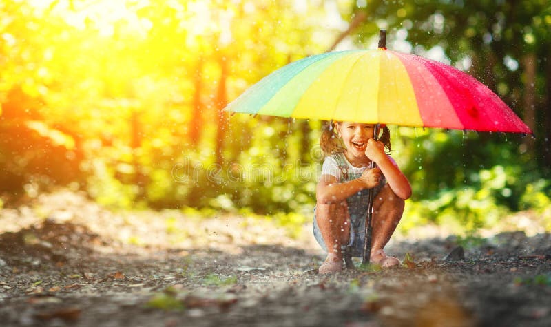 A menina feliz da criança ri e joga sob a chuva do verão com um umbr fotografia de stock A menina feliz da criança ri e joga sob a chuva do verão com um umbr fotografia de stock