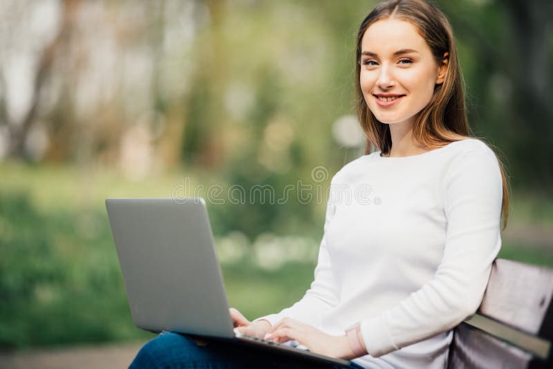 Menina feliz do adolescente do estudante que aprende com um portátil que encontra-se em um banco em um campus universitário fotografia de stock royalty free Menina feliz do adolescente do estudante que aprende com um portátil que encontra-se em um banco em um campus universitário fotografia de stock royalty free