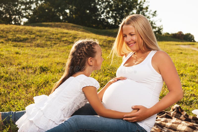 Menina feliz que abraça a barriga grávida da sua mãe foto de stock royalty free Menina feliz que abraça a barriga grávida da sua mãe foto de stock royalty free