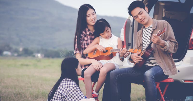 Menina feliz que joga a uquelele com a família asiática que senta-se em t imagens de stock Menina feliz que joga a uquelele com a família asiática que senta-se em t imagens de stock
