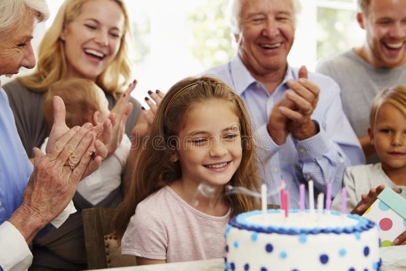 A menina funde para fora velas do bolo de aniversário no partido da família foto de stock A menina funde para fora velas do bolo de aniversário no partido da família foto de stock