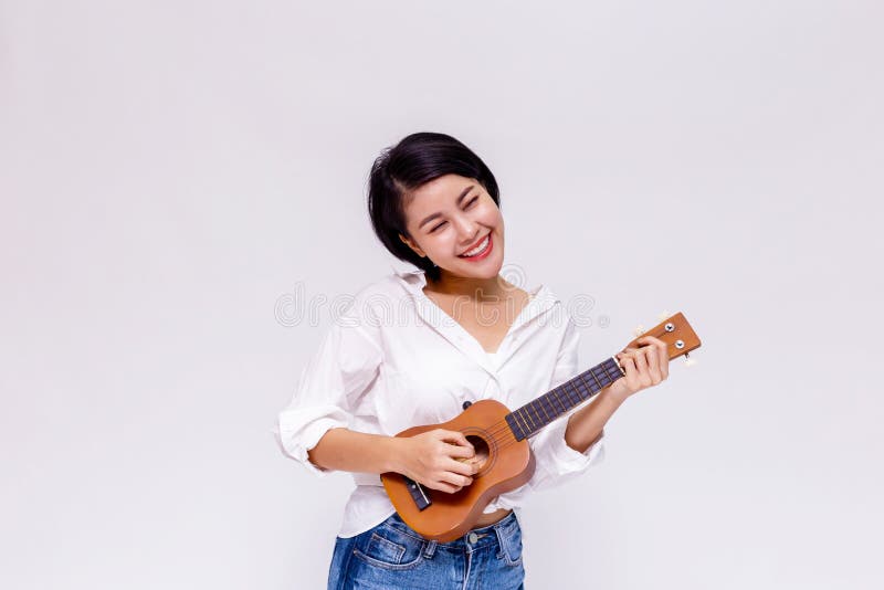 Menina fêmea asiática nova que joga a guitarra da praia da uquelele no fundo isolado branco imagens de stock royalty free Menina fêmea asiática nova que joga a guitarra da praia da uquelele no fundo isolado branco imagens de stock royalty free
