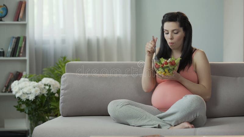 Menina grávida eternalmente com fome que come a salada, saturando o corpo com vitaminas