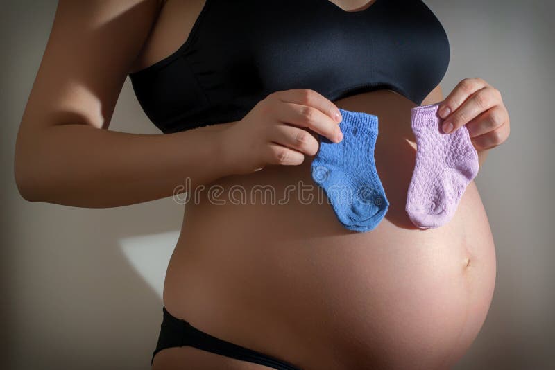 A menina grávida que guarda o bebê colorido golpeia perto de sua barriga imagem de stock royalty free A menina grávida que guarda o bebê colorido golpeia perto de sua barriga imagem de stock royalty free