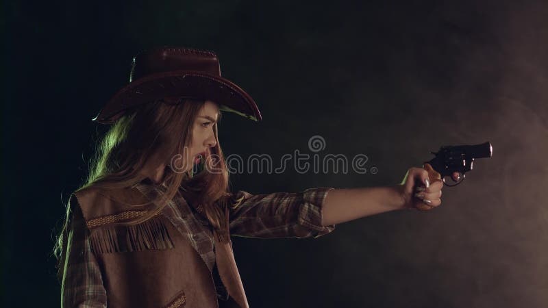 A menina guarda um revólver em suas mãos e em visar o bandido Fundo preto do fumo Movimento lento Vista lateral