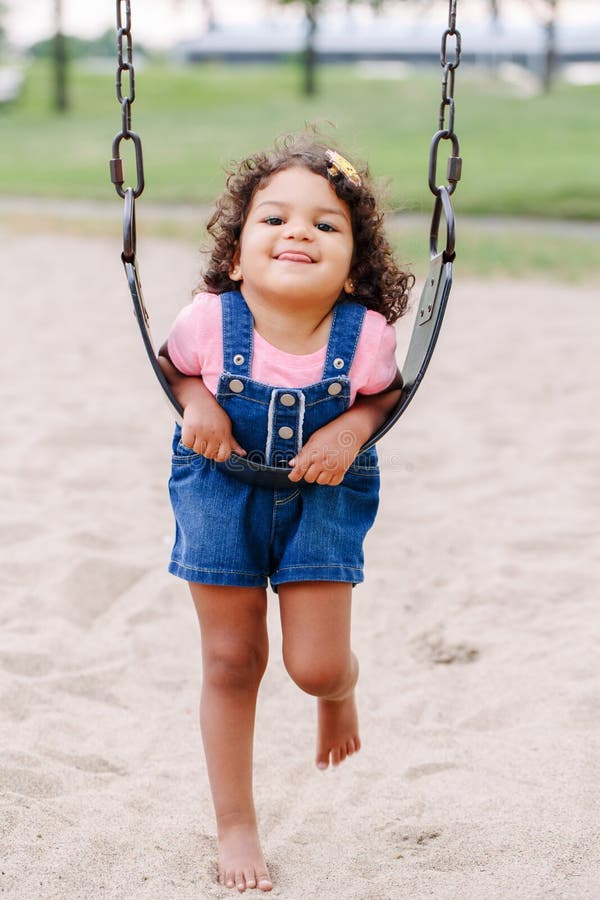 Menina latino-americano da criança do latino pequeno que balança em balanços no campo de jogos fora no dia de verão fotos de stock Menina latino-americano da criança do latino pequeno que balança em balanços no campo de jogos fora no dia de verão fotos de stock