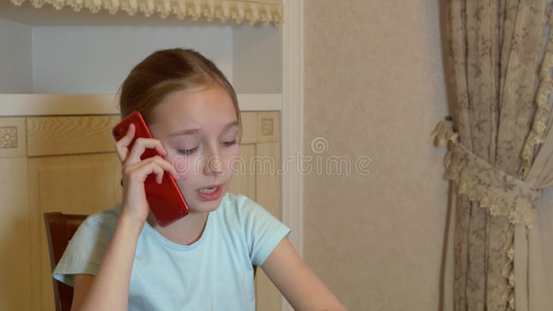Menina linda séria sentada em casa e falando por smartphone