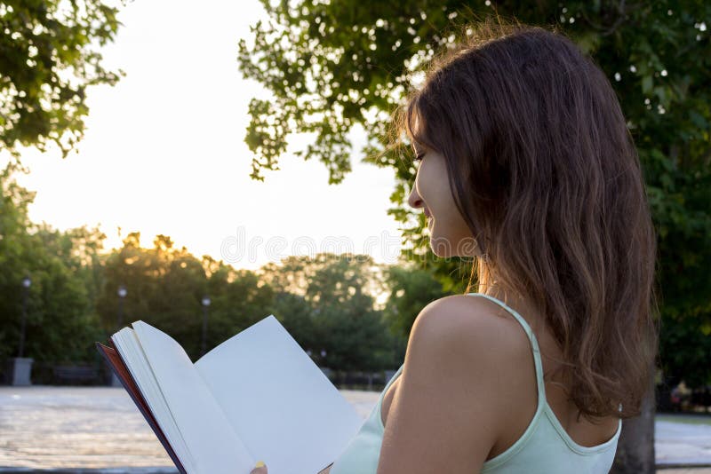 A menina lindo aprecia ler um livro e o por do sol O estudante fêmea está preparando-se para o exame ou o teste fora imagem de stock A menina lindo aprecia ler um livro e o por do sol O estudante fêmea está preparando-se para o exame ou o teste fora imagem de stock
