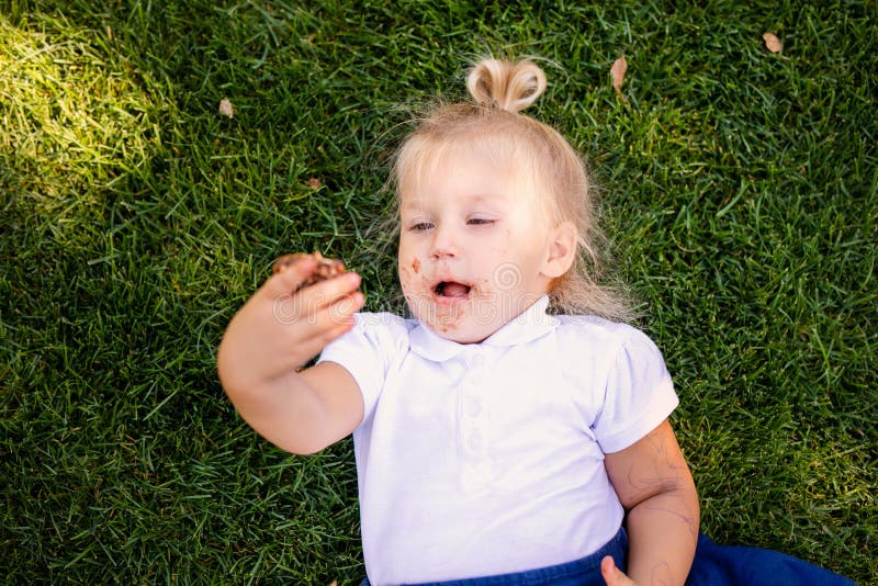 Feliz Bebê Loira Com Duas Pequenas Tranças Em Camiseta Branca E Um Kit De  Calças Jeans Sentado Sobre O Fundo Da Grama Verde Foto de Stock - Imagem de  pouco, inocência: 143643548