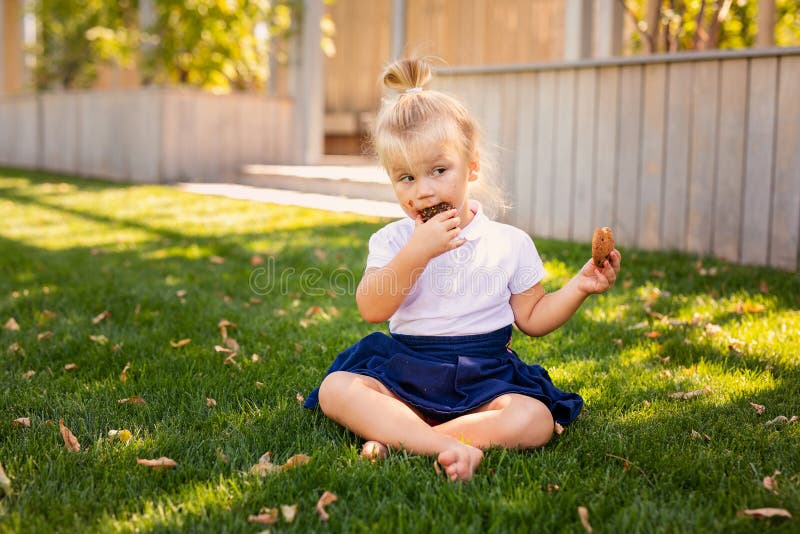 Feliz Bebê Loira Com Duas Pequenas Tranças Em Camiseta Branca E Um Kit De  Calças Jeans Sentado Sobre O Fundo Da Grama Verde Foto de Stock - Imagem de  pouco, inocência: 143643548