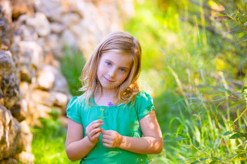 Menina loura da criança que sorri com o exterior relaxado da flor roxa foto de stock Menina loura da criança que sorri com o exterior relaxado da flor roxa foto de stock