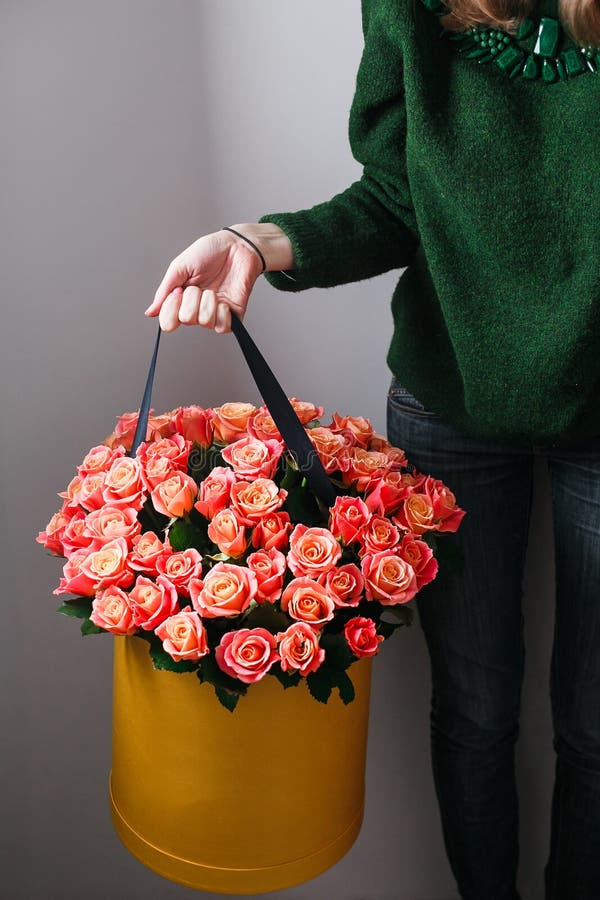 Menina loura nova agradável cheirando floresce mantendo o ramalhete das rosas do pêssego na caixa do chapéu contra a parede empla imagem de stock royalty free Menina loura nova agradável cheirando floresce mantendo o ramalhete das rosas do pêssego na caixa do chapéu contra a parede empla imagem de stock royalty free