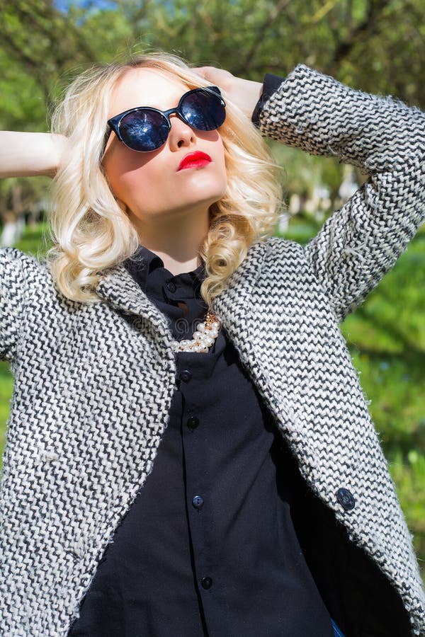 Menina loura 'sexy' bonita com os bordos vermelhos nos óculos de sol que anda no jardim de um dia ensolarado brilhante fotografia de stock Menina loura 'sexy' bonita com os bordos vermelhos nos óculos de sol que anda no jardim de um dia ensolarado brilhante fotografia de stock