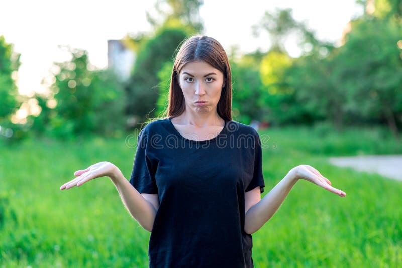 A menina moreno No verão no ar livre Em um t-shirt preto no gramado verde Frustração da frustração da emoção imagem de stock A menina moreno No verão no ar livre Em um t-shirt preto no gramado verde Frustração da frustração da emoção imagem de stock