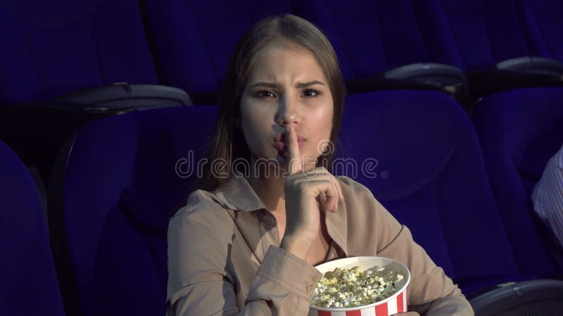 A menina mostra um sinal do silêncio que senta-se no salão do cinema imagem de stock royalty free A menina mostra um sinal do silêncio que senta-se no salão do cinema imagem de stock royalty free
