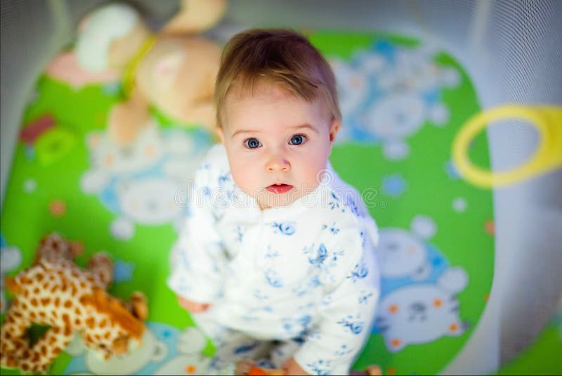 Menina muito bonito nos pijamas que sentam-se no cercadinho fotografia de stock Menina muito bonito nos pijamas que sentam-se no cercadinho fotografia de stock