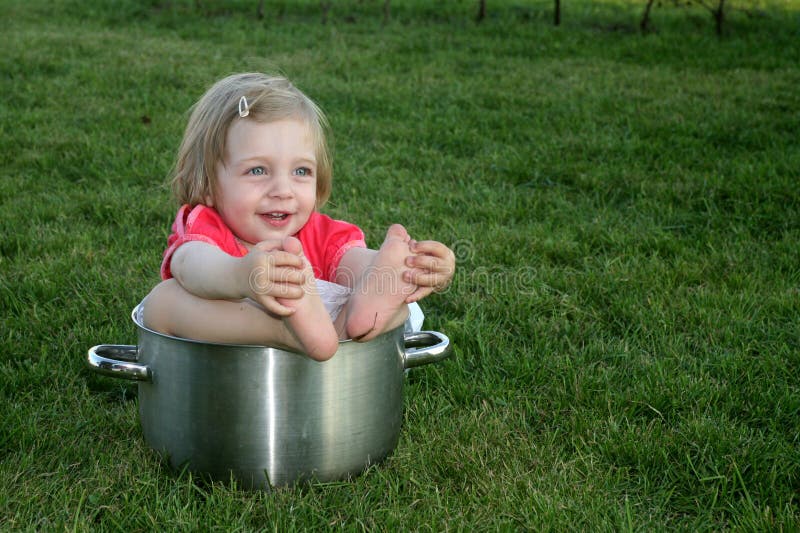 A cute little girl sitting in a big pot on the grass. A cute little girl sitting in a big pot on the grass