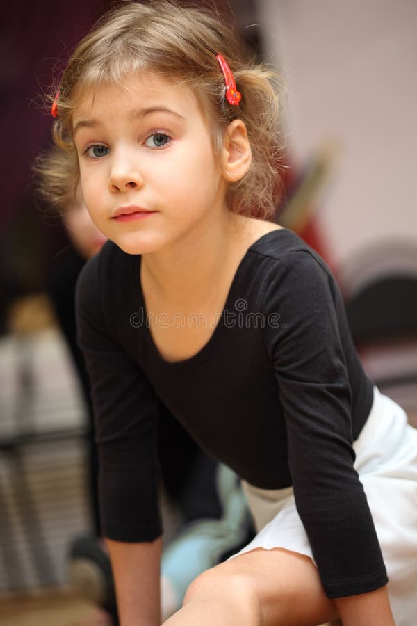 Little girl in ballet class sits on string on floor and looks into camera. Little girl in ballet class sits on string on floor and looks into camera