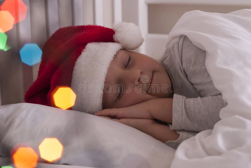 Menina no chapéu de Santa na cama foto de stock royalty free Menina no chapéu de Santa na cama foto de stock royalty free