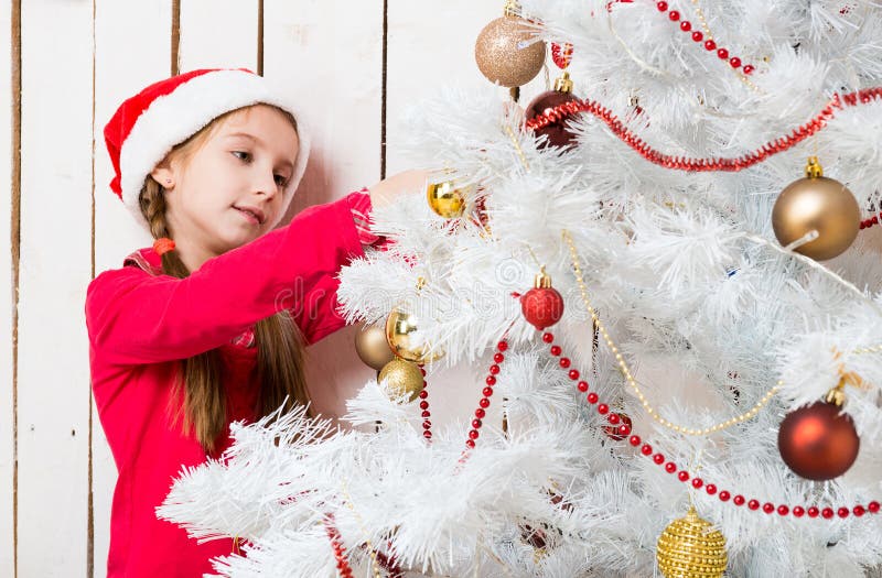 Menina no chapéu vermelho de Santa que decora a árvore do ano novo fotografia de stock royalty free Menina no chapéu vermelho de Santa que decora a árvore do ano novo fotografia de stock royalty free