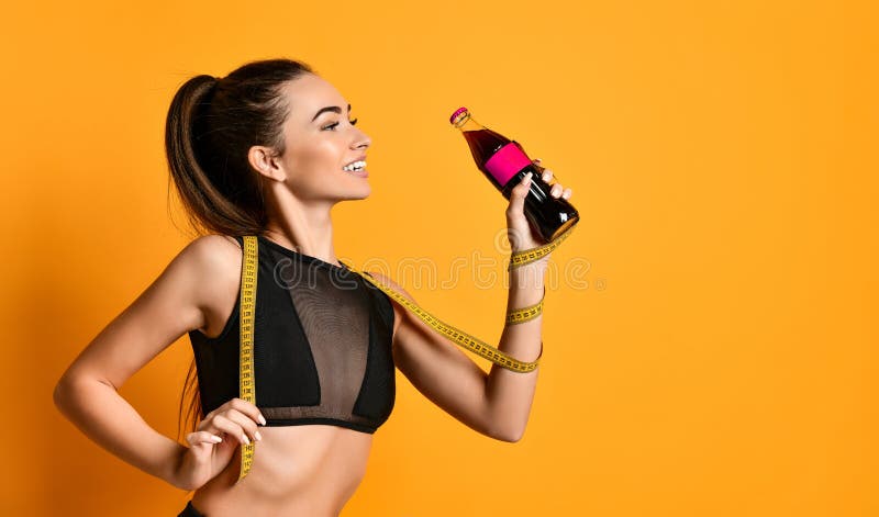 Nice young fitness girl in black sportswear is looking at the camera and keeps at hand a tape measure and a bottle of sports nutrition liquid. Healthy life weight loss concept. Nice young fitness girl in black sportswear is looking at the camera and keeps at hand a tape measure and a bottle of sports nutrition liquid. Healthy life weight loss concept