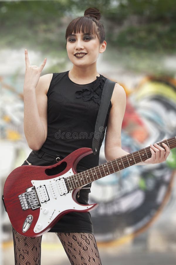 Menina nova do punk rock que dá chifres do diabo com sua mão e que guardara a guitarra fotos de stock Menina nova do punk rock que dá chifres do diabo com sua mão e que guardara a guitarra fotos de stock