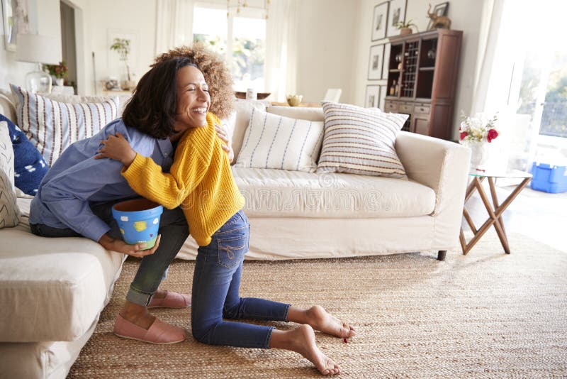 menina Pre-adolescente que abraça sua mãe na sala de estar após ter dado lhe um presente feito a mão, vista lateral imagens de stock royalty free menina Pre-adolescente que abraça sua mãe na sala de estar após ter dado lhe um presente feito a mão, vista lateral imagens de stock royalty free