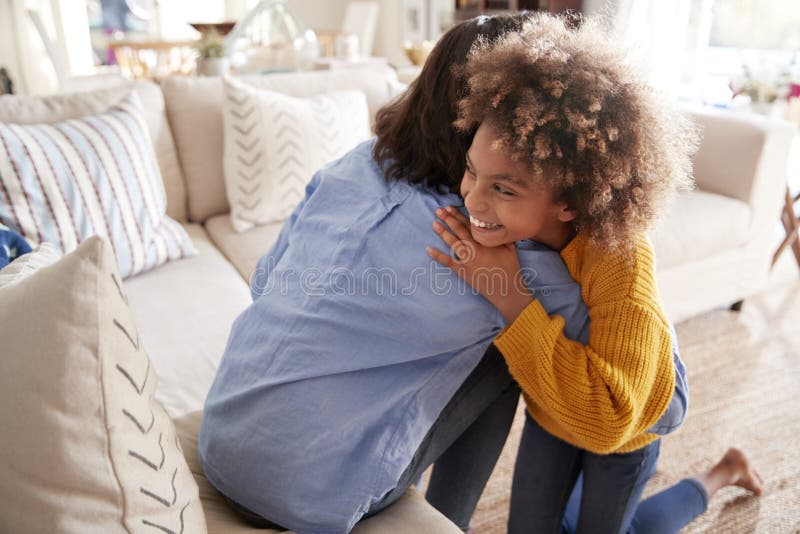 menina Pre-adolescente que abraça sua mãe que senta-se no sofá na sala de visitas, vista elevada, traseira fotos de stock menina Pre-adolescente que abraça sua mãe que senta-se no sofá na sala de visitas, vista elevada, traseira fotos de stock
