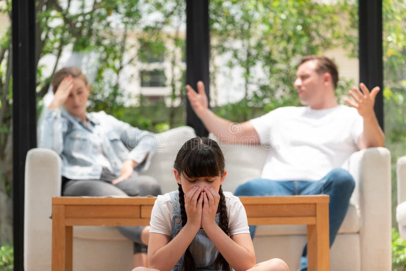 Stressed and unhappy young girl crying and trapped in middle of tension by her parent argument in living room. Unhealthy domestic lifestyle and traumatic childhood develop to depression. Synchronos. Stressed and unhappy young girl crying and trapped in middle of tension by her parent argument in living room. Unhealthy domestic lifestyle and traumatic childhood develop to depression. Synchronos