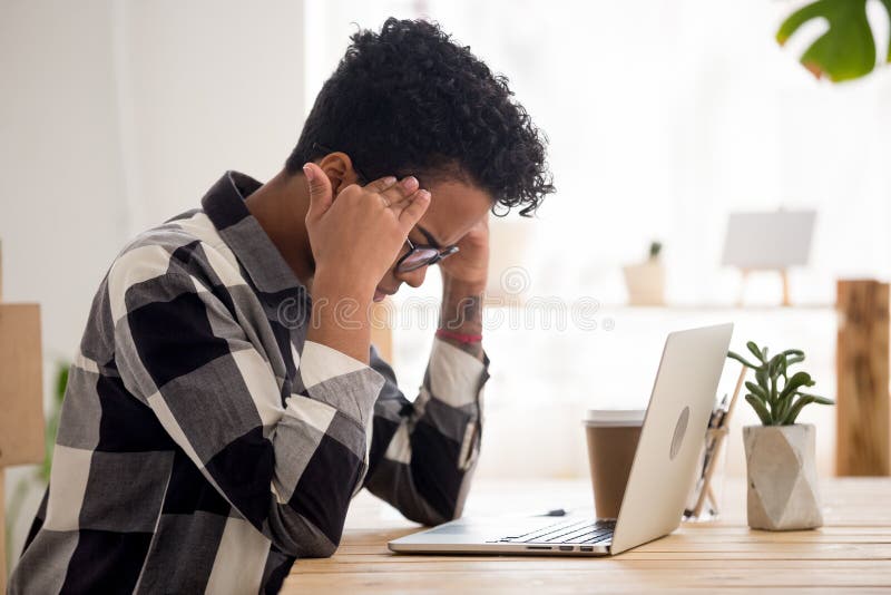 Menina preta esgotada para sofrer da enxaqueca no local de trabalho imagem de stock Menina preta esgotada para sofrer da enxaqueca no local de trabalho imagem de stock