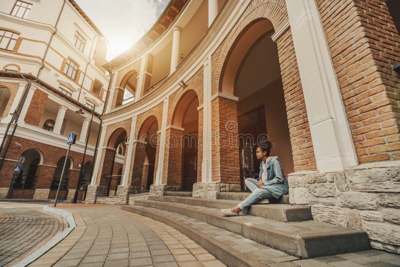 Menina preta que senta-se na escadaria em ajustes urbanos imagem de stock Menina preta que senta-se na escadaria em ajustes urbanos imagem de stock