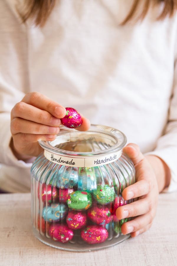 A menina que abre um frasco da folha colorida envolveu doces dos ovos de chocolate imagens de stock A menina que abre um frasco da folha colorida envolveu doces dos ovos de chocolate imagens de stock