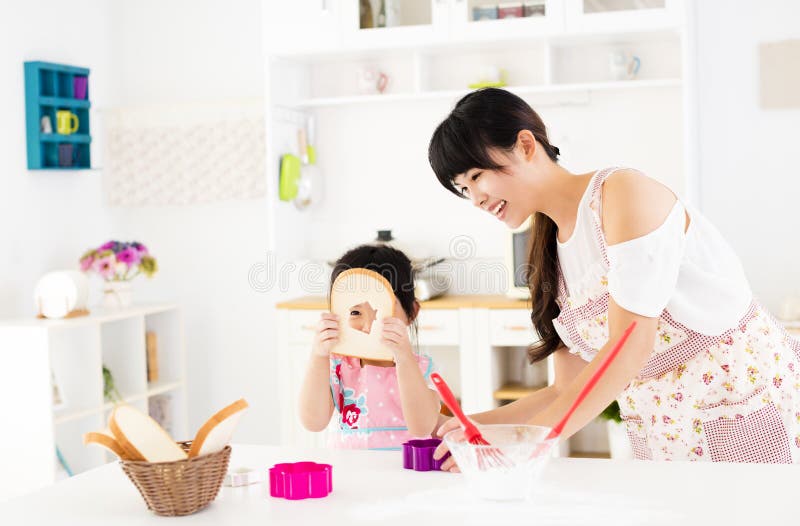 A menina que ajuda sua mãe prepara o alimento na cozinha foto de stock A menina que ajuda sua mãe prepara o alimento na cozinha foto de stock