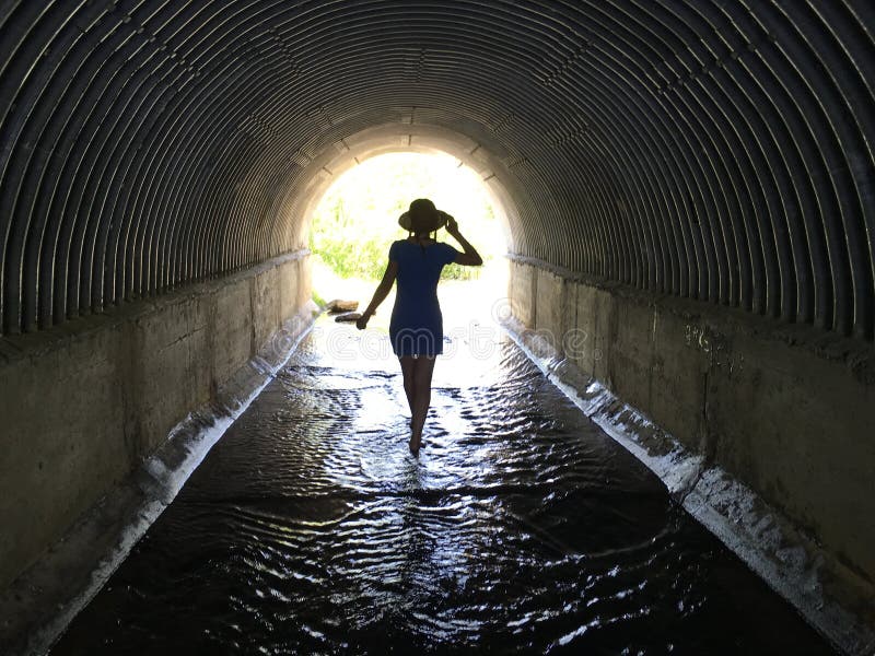 Menina que anda com os pés descalços através da água em um túnel escuro à luz foto de stock royalty free Menina que anda com os pés descalços através da água em um túnel escuro à luz foto de stock royalty free