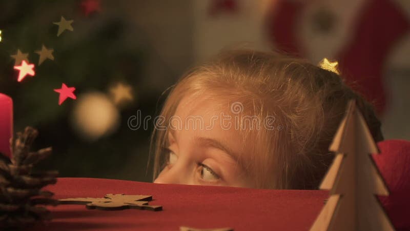 Menina que aparece de debaixo da tabela, olhando ao redor, fazendo partidas do Natal