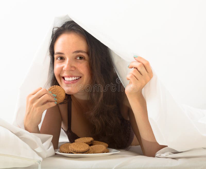 Menina a comer biscoitos na cama fotos de stock royalty free