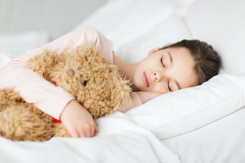 Menina que dorme com o brinquedo do urso de peluche na cama em casa