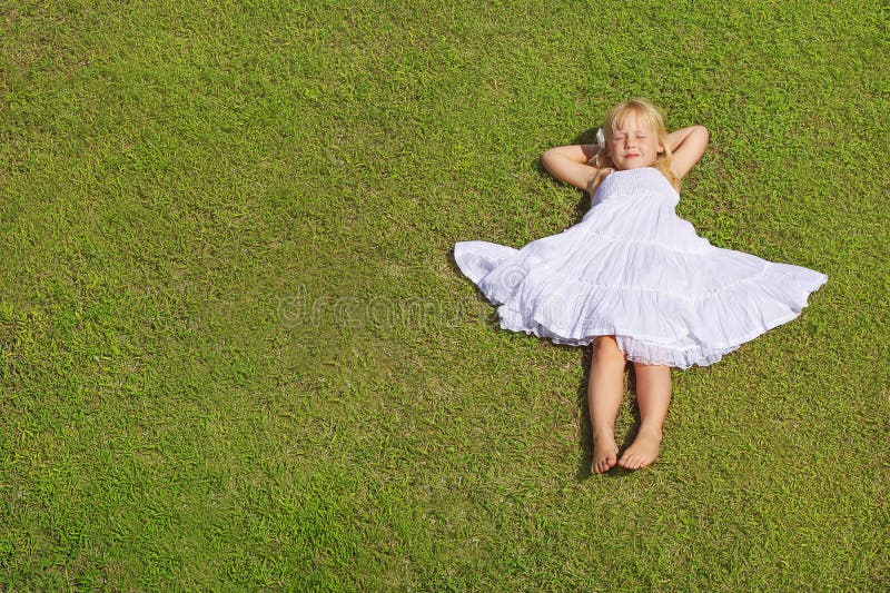 Menina que encontra-se na grama verde, vista superior da criança bonita imagem de stock Menina que encontra-se na grama verde, vista superior da criança bonita imagem de stock