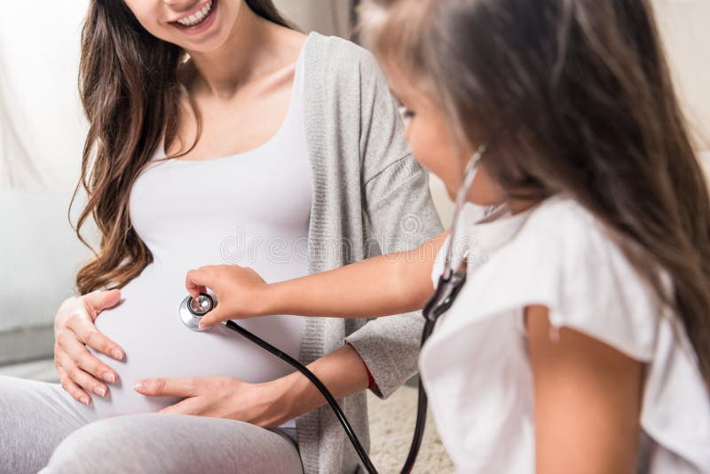 Menina que escuta a barriga grávida através do estetoscópio fotos de stock Menina que escuta a barriga grávida através do estetoscópio fotos de stock