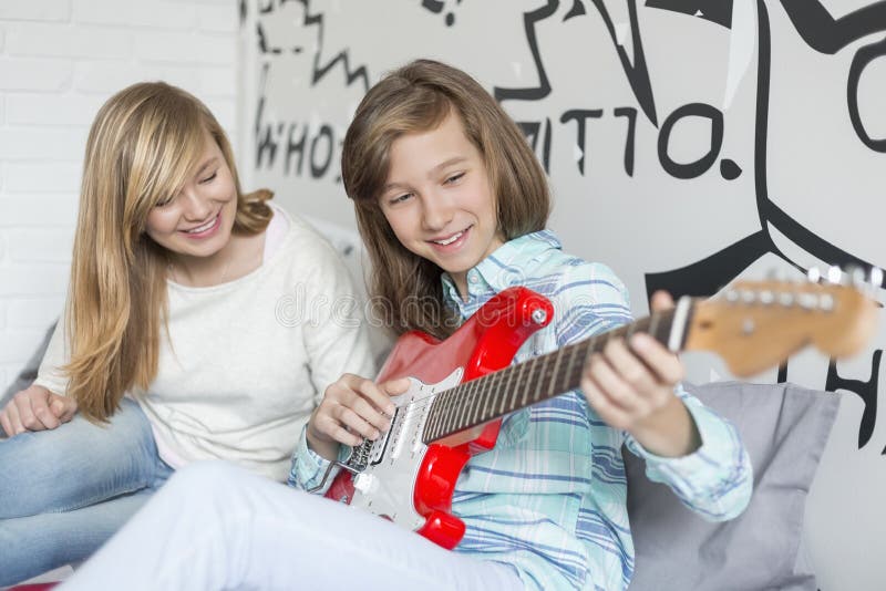 Menina que escuta a irmã que joga a guitarra em casa imagem de stock Menina que escuta a irmã que joga a guitarra em casa imagem de stock