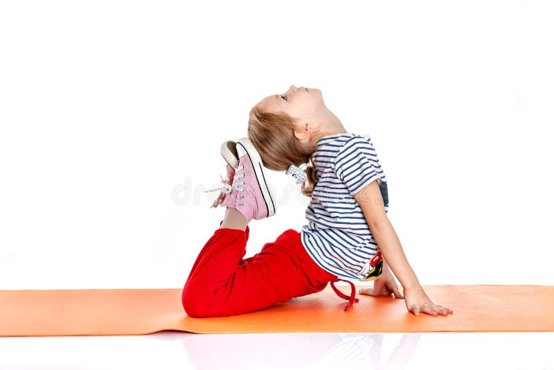 Menina que faz exercícios ginásticos em uma esteira alaranjada da ioga doi fotografia de stock royalty free Menina que faz exercícios ginásticos em uma esteira alaranjada da ioga doi fotografia de stock royalty free