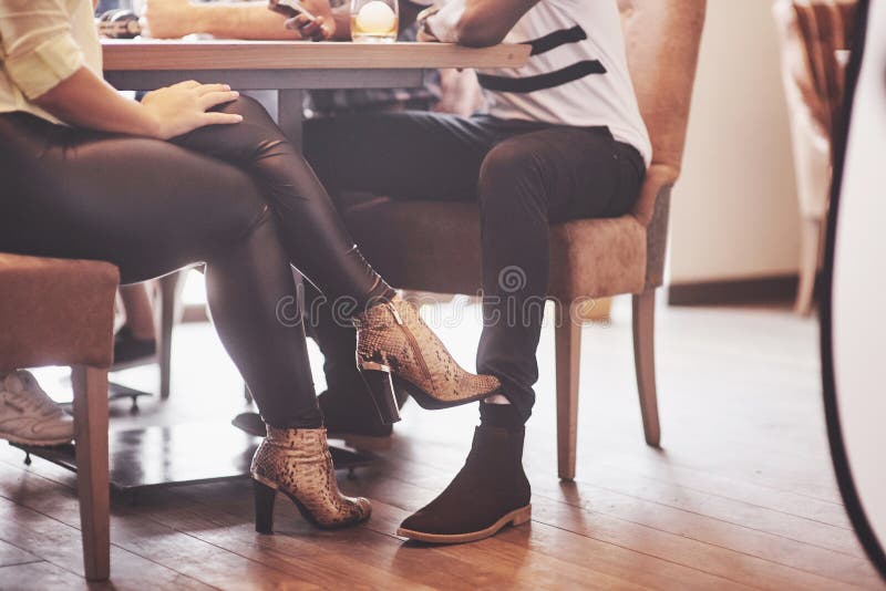 Menina que flerta com um pé tocante do indivíduo seu pé sob a tabela em um café ao ter o divertimento com os amigos Namoradeira c fotos de stock Menina que flerta com um pé tocante do indivíduo seu pé sob a tabela em um café ao ter o divertimento com os amigos Namoradeira c fotos de stock