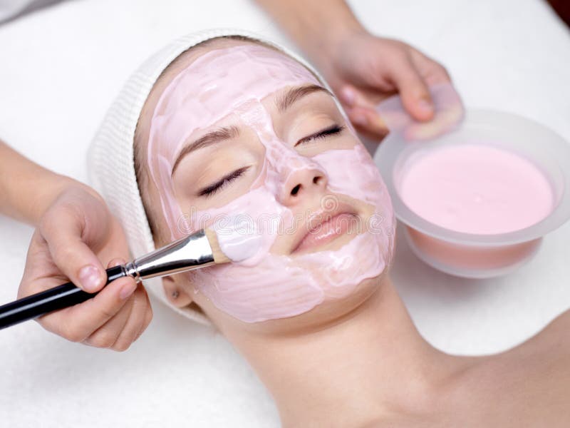 Menina que recebe a máscara facial cor-de-rosa cosmética