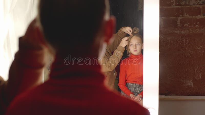 Menina que recebe penteado no estúdio de cabeleireiro espelho frontal Moda estilista fazendo hairdo para adolescente