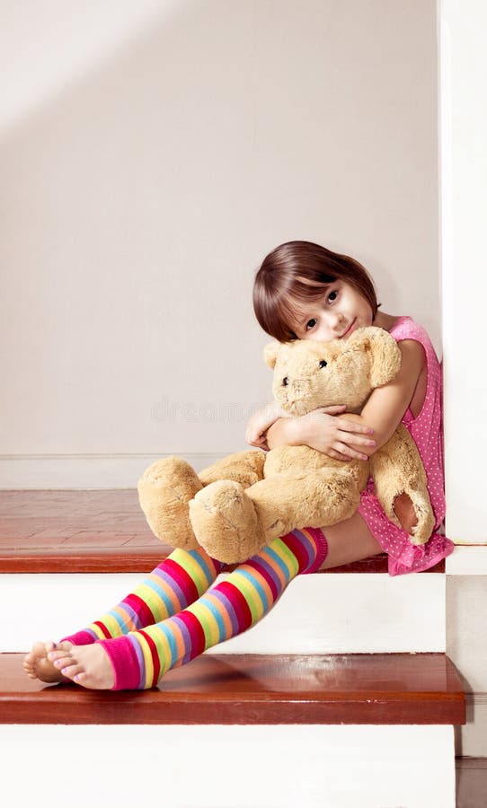 Menina que senta e que guarda o urso de peluche fotografia de stock royalty free Menina que senta e que guarda o urso de peluche fotografia de stock royalty free