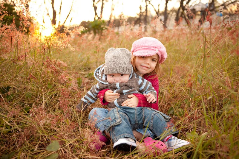 Little girl sits and holds her baby brother in a countryside field of grass. Horizontal shot. Little girl sits and holds her baby brother in a countryside field of grass. Horizontal shot.