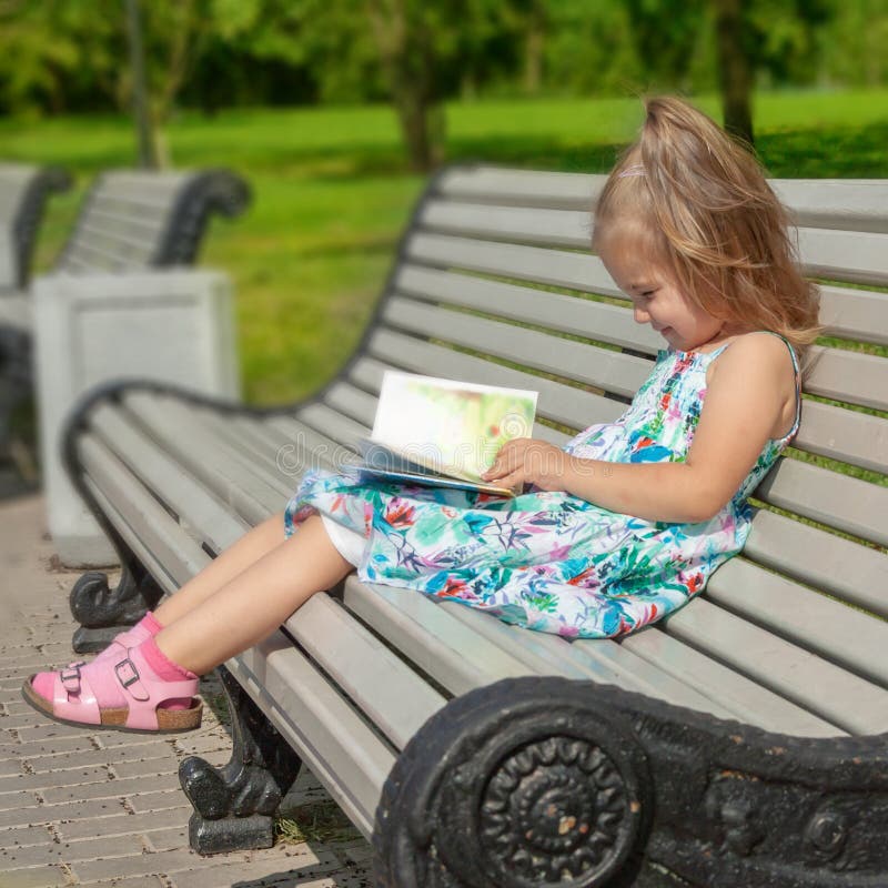 A menina senta-se em um banco no parque e lê-se o livro imagens de stock A menina senta-se em um banco no parque e lê-se o livro imagens de stock