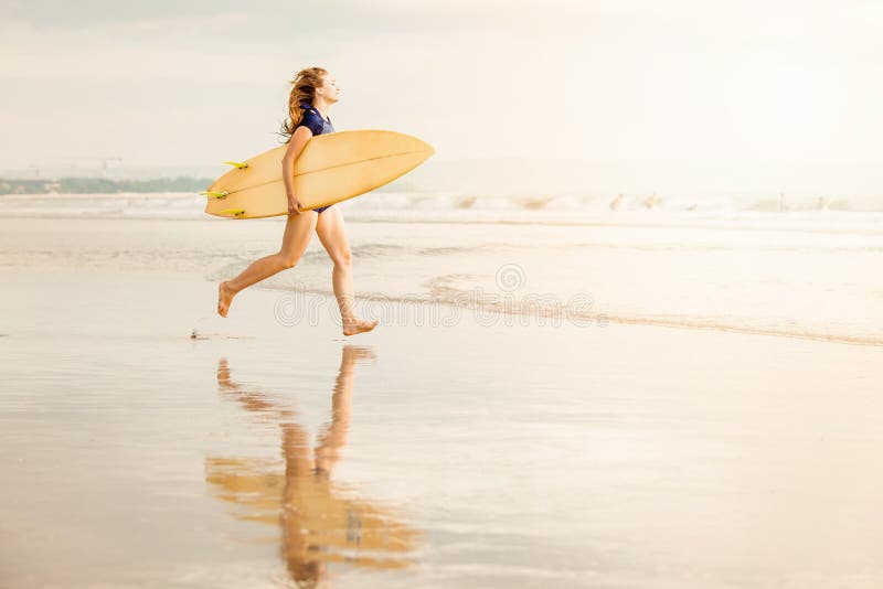 Beautiful surfer girl on the beach at sunset running into ocean with yellow surfboard in her hands in sunset light. Healthy life, sport concept with copyspace. Beautiful surfer girl on the beach at sunset running into ocean with yellow surfboard in her hands in sunset light. Healthy life, sport concept with copyspace