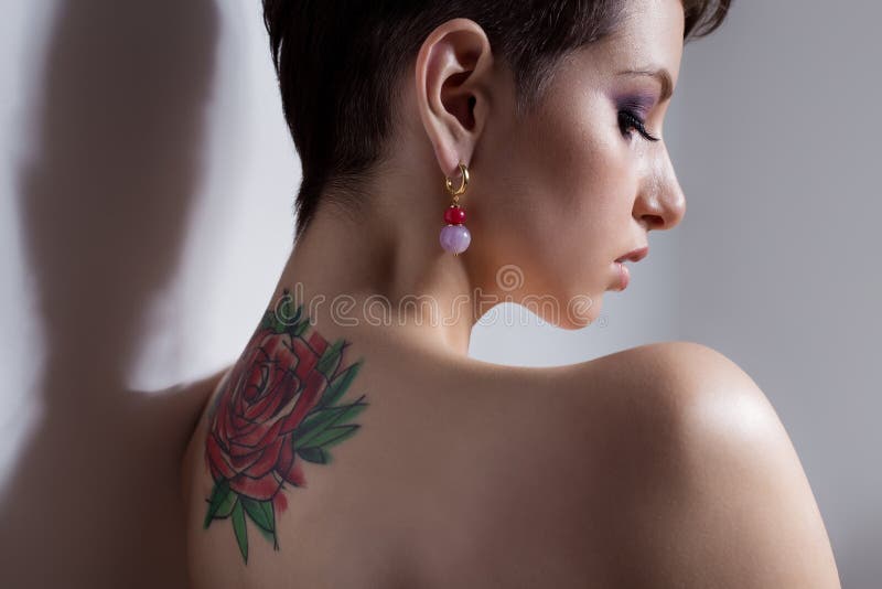 A menina 'sexy' nova bonita com cabelo curto com tatuagem no seu para trás está contra a parede com os ombros desencapados triste imagens de stock royalty free A menina 'sexy' nova bonita com cabelo curto com tatuagem no seu para trás está contra a parede com os ombros desencapados triste imagens de stock royalty free